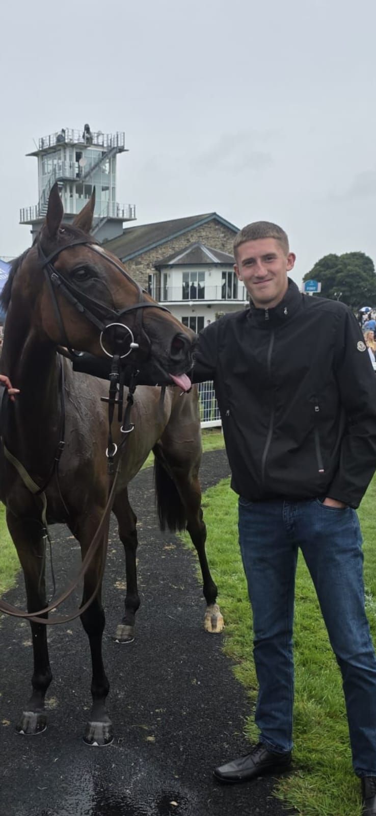Team member standing beside a playful bay racehorse during a race-day visit