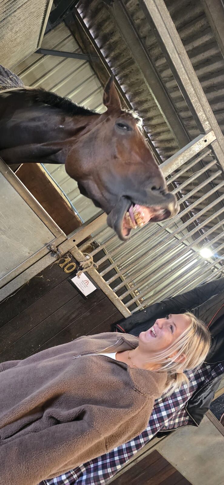 A horse makes a comical face beside a smiling member of the yard staff.